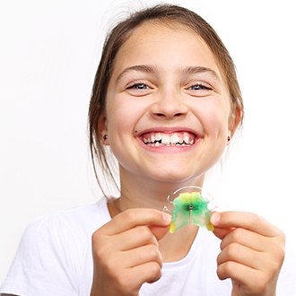 Smiling girl holding up an orthodontic appliance