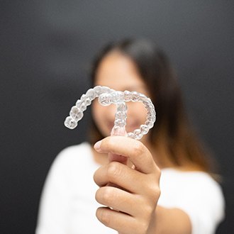 Smiling patient holding up Invisalign in Holliston