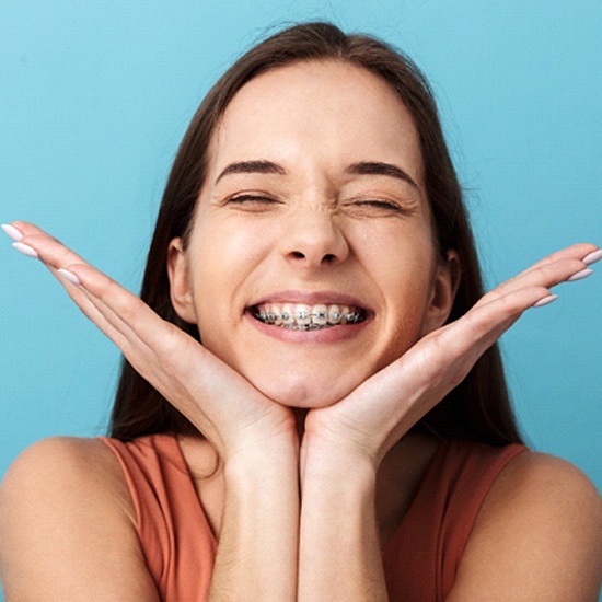 A young girl smiling with her eyes closed while holding her head between her hands