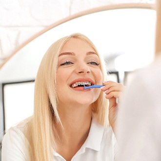 A young woman with blonde hair using an interdental brush to properly clean between their teeth and underneath their archwire