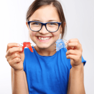 Smiling girl holding up orthodontic appliances