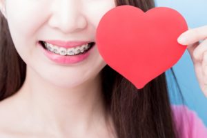 Young woman with braces in Holliston smiles with paper heart