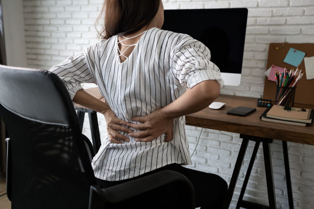 Woman experiencing back pain in work chair